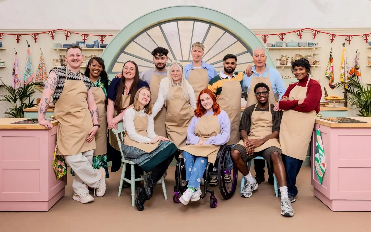 The twelve Series 17 bakers in beige aprons, gathered in front of the tent's arched window